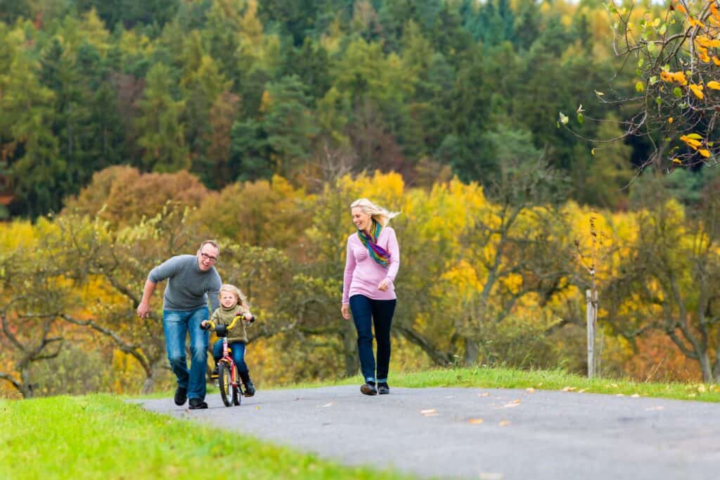 A young girl is learning to use the bike with her father and mother in a park